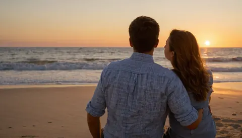 A couple sitting on a beach watching the sunset over the ocean.