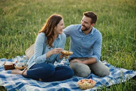 A happy couple enjoying a picnic on a blue plaid blanket in a grassy field.