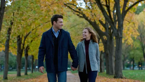 A man and woman holding hands and smiling while walking through an autumn park.