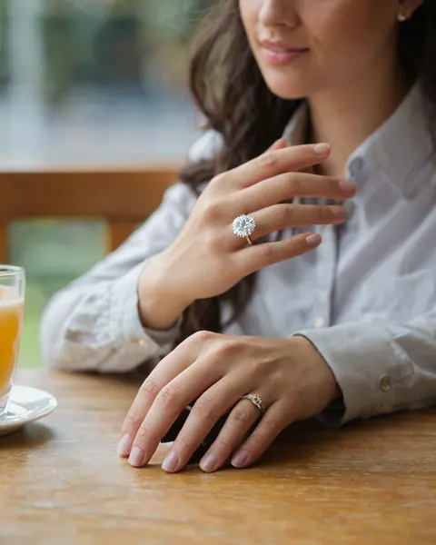 A woman showing off her engagement ring at a cafe table with orange juice