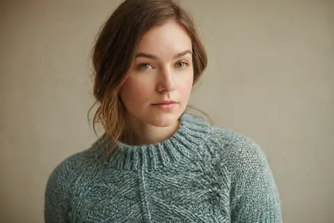 Woman in teal knit sweater with brown hair and green eyes against beige background